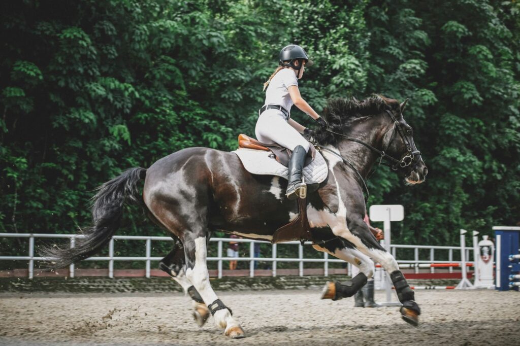 Woman riding a horse at a barn near trees.