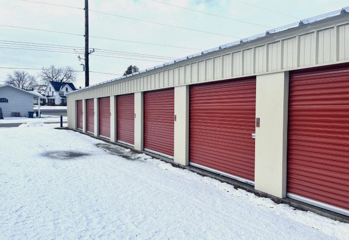 light beige mini storage row with red doors, snow covering ground in front